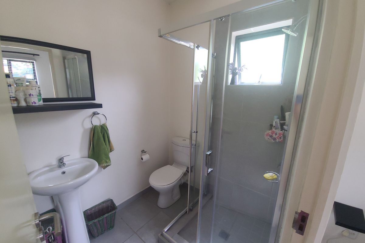 A functional bathroom featuring a pedestal basin, a toilet, and a glass-enclosed shower with tiled flooring and natural light from a window.
