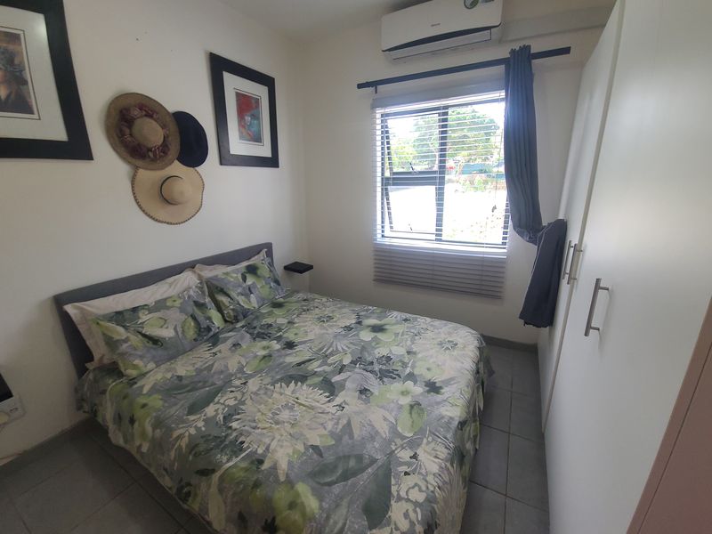 A compact bedroom featuring tiled flooring, a built-in wardrobe, and a wall-mounted split-system air conditioner.