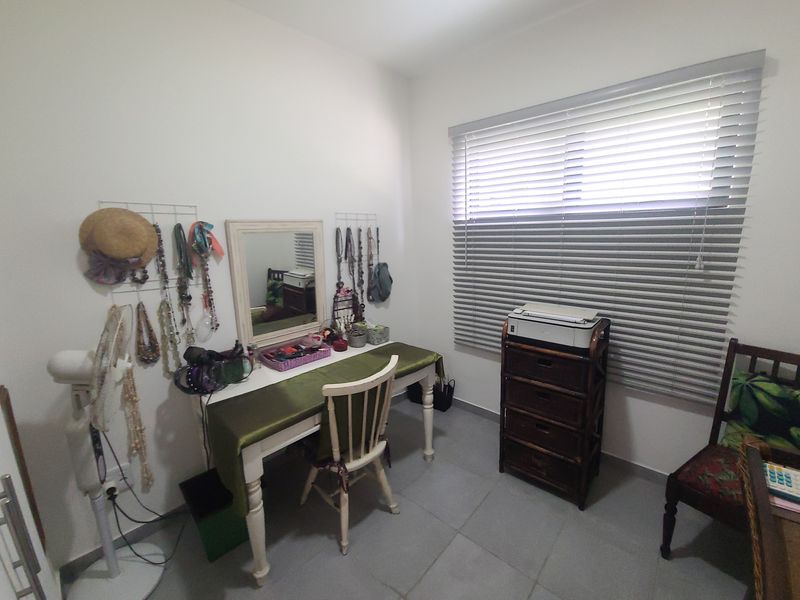 A functional bedroom space featuring neutral wall finishes, tiled flooring, and adjustable venetian blinds for privacy and light control.