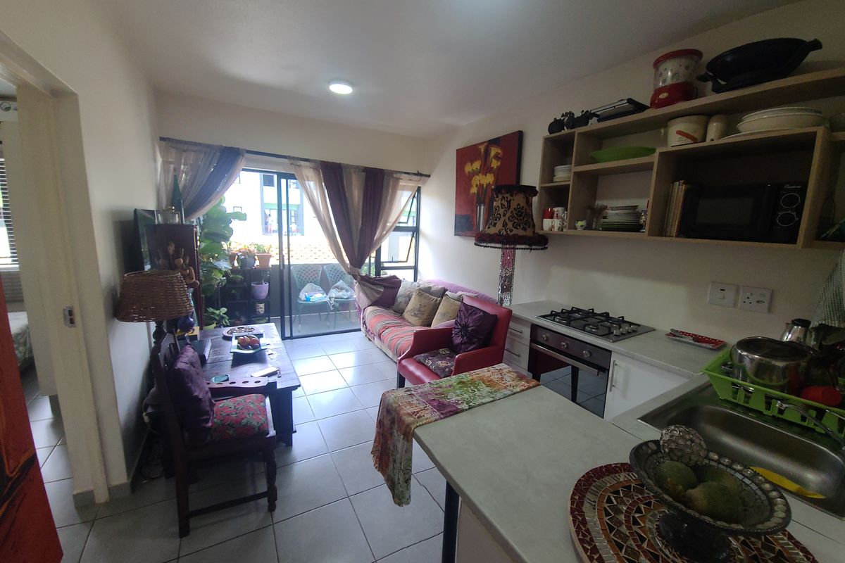 Open-plan living area featuring a functional kitchen with gas hob, oven, and tiled flooring, leading directly to a balcony through sliding glass doors.
