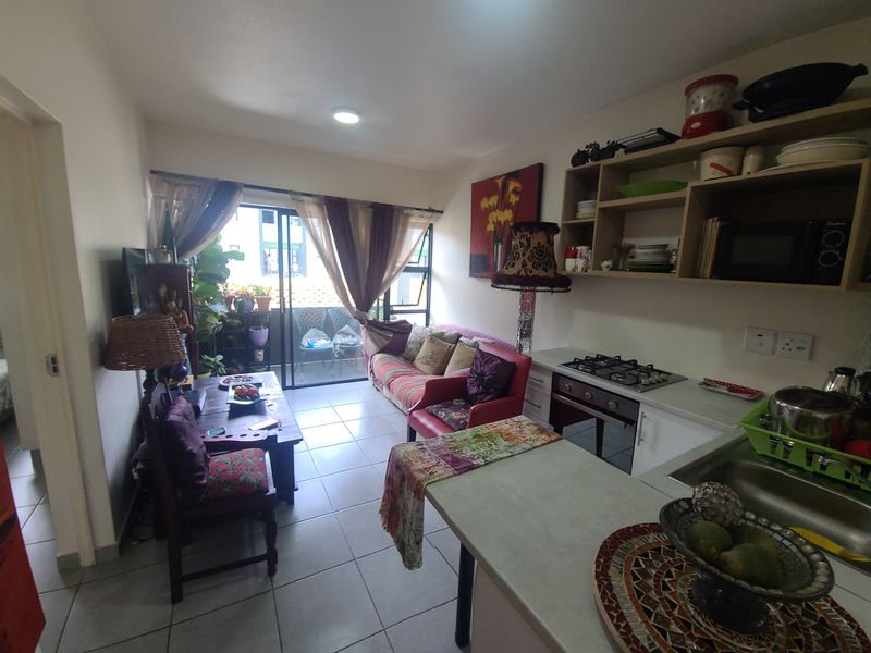 Open-plan living area featuring a functional kitchen with gas hob, oven, and tiled flooring, leading directly to a balcony through sliding glass doors.