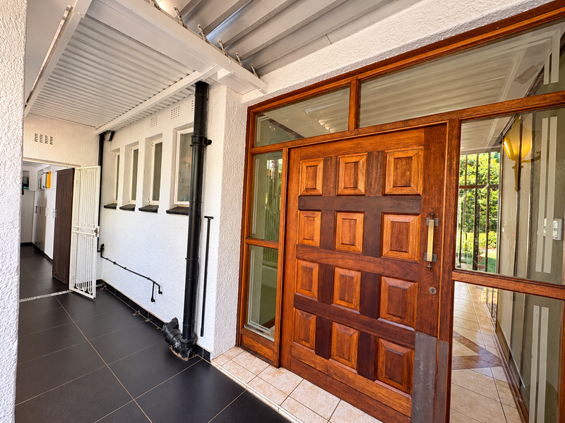 A covered entrance area featuring a substantial solid timber panelled front door, tiled flooring, and a metal security gate leading into the home.