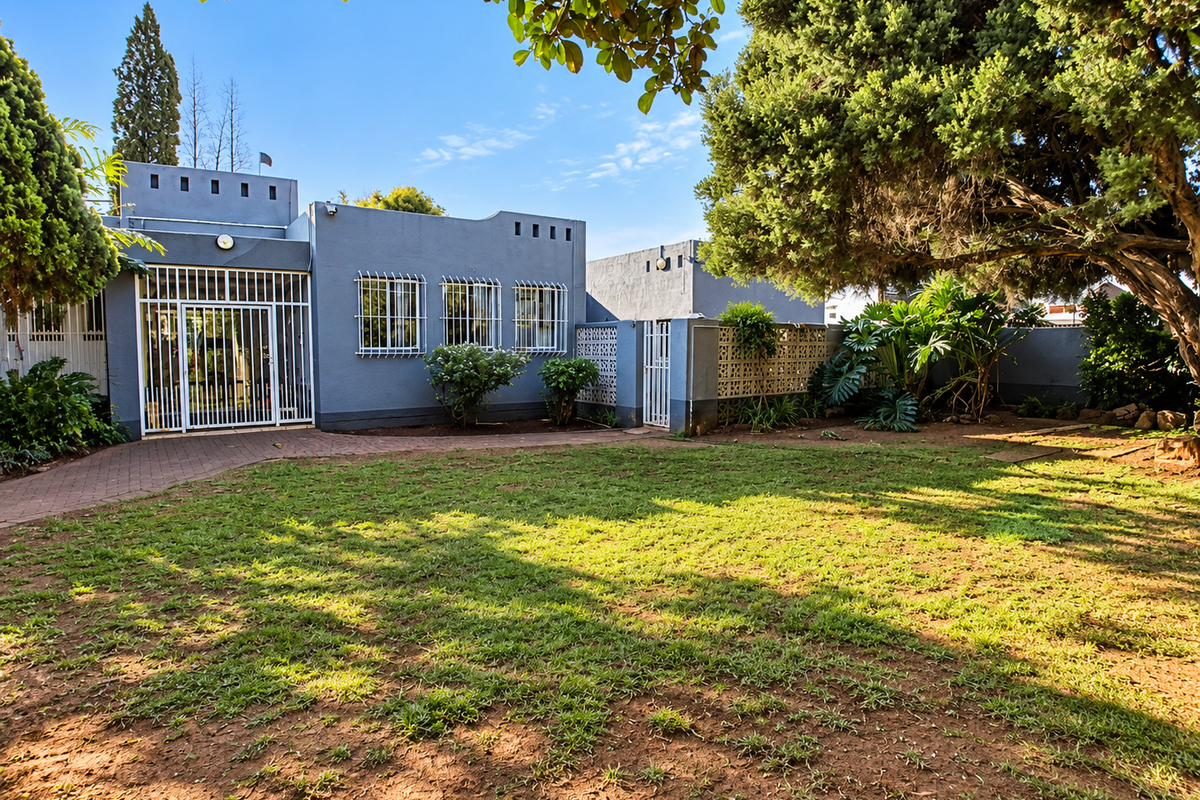 A view of the rear garden featuring a paved walkway, established trees, and a secure entrance with security bars and gates.