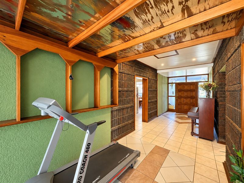 Spacious entrance hallway featuring a unique timber beam ceiling, textured brick walls, and durable ceramic floor tiles leading to the main living areas.