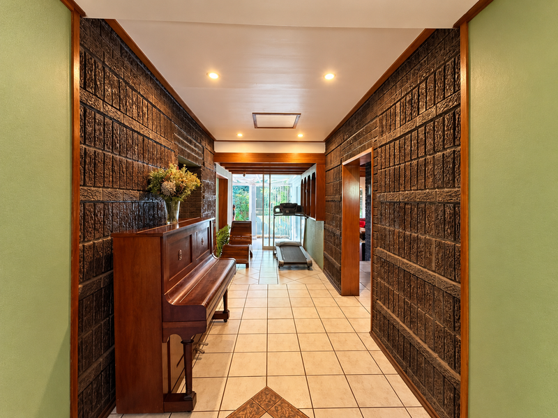 Spacious hallway featuring distinctive textured brick walls, ceramic tile flooring, and recessed lighting, creating a unique architectural transition space within the home.
