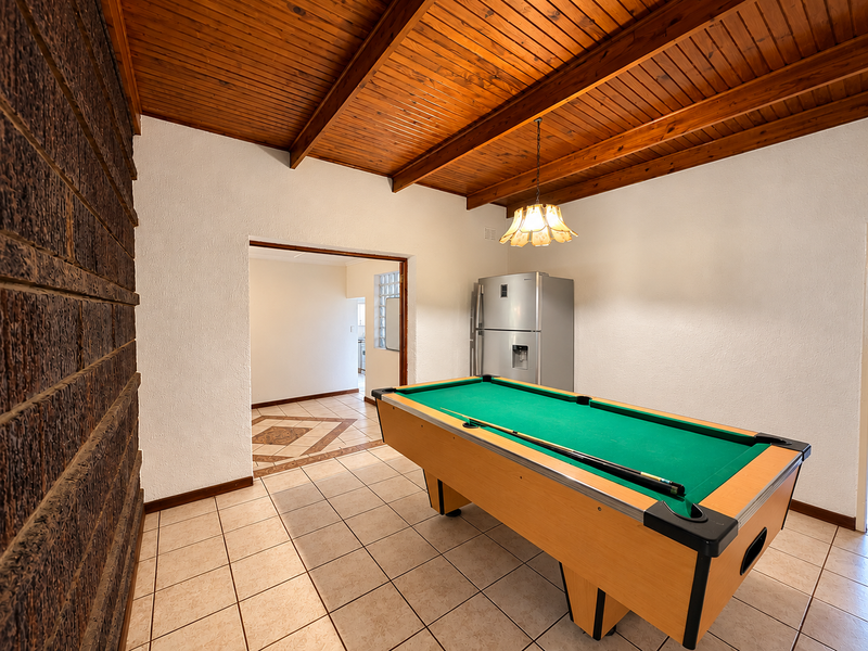 Living area featuring a distinctive exposed timber beam ceiling, feature brick wall, and ceramic floor tiles, offering a rustic and character-filled space.