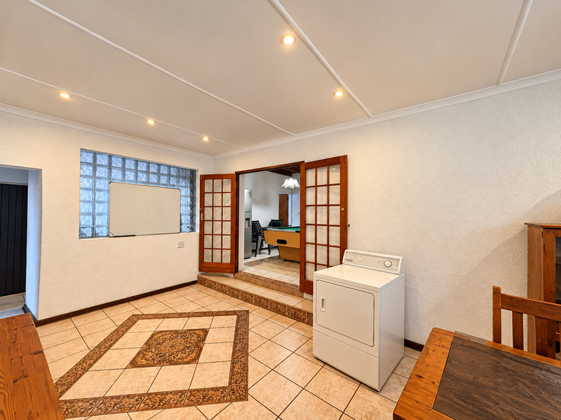 A functional laundry area featuring tiled flooring with decorative inlay, glass block window, and timber-framed double doors leading to an adjacent room.