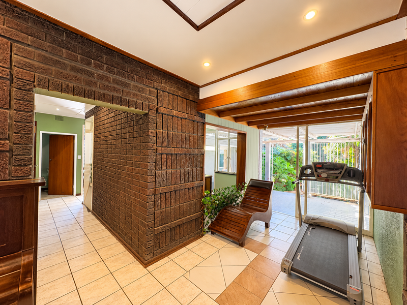 A living area featuring an exposed brick wall, timber ceiling beams, and direct access to an outdoor patio through sliding glass doors.