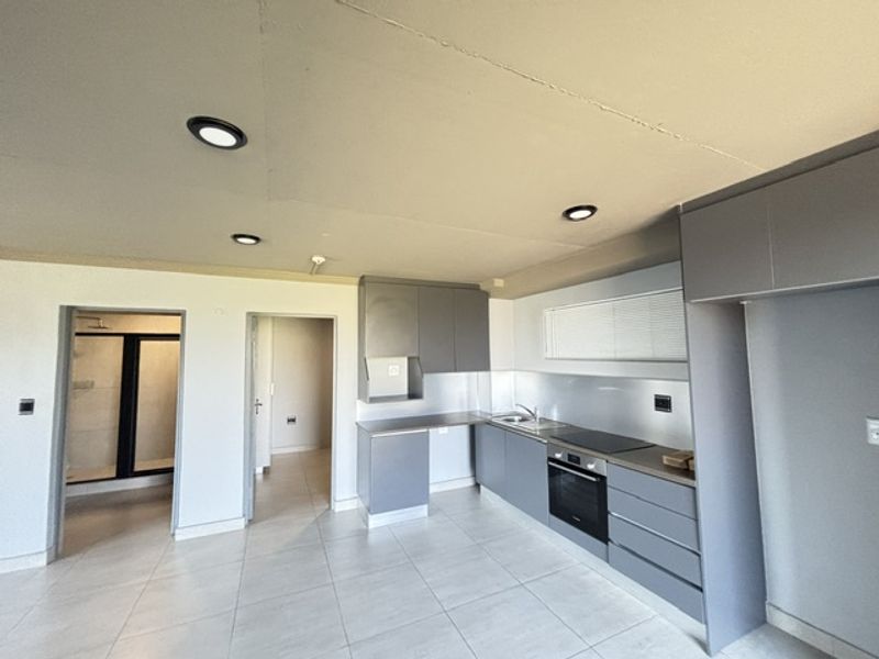 An open-plan kitchen area featuring modern grey cabinetry, integrated appliances, and tiled flooring, with direct access to adjacent rooms.