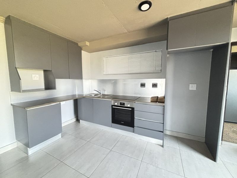 Modern kitchen featuring sleek grey cabinetry, stainless steel splashback, integrated oven and hob, and tiled flooring in a clean, minimalist layout.