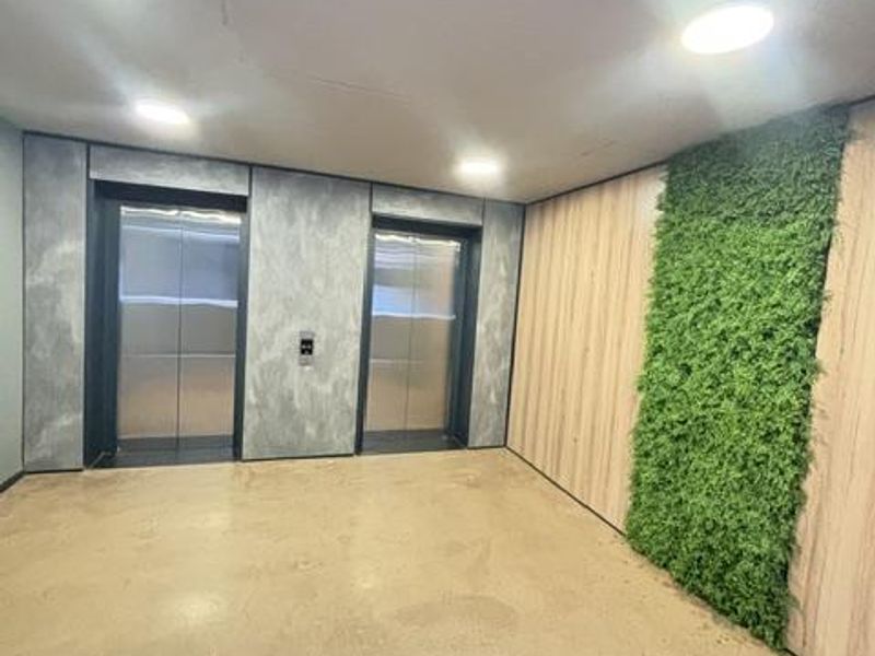 Modern apartment building lobby featuring dual elevators, polished concrete flooring, and a decorative vertical garden wall.
