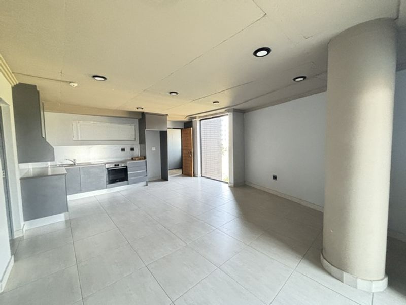 Spacious open-plan living and kitchen area featuring modern grey cabinetry, integrated oven, tiled flooring, and recessed lighting in a clean, vacant setting.