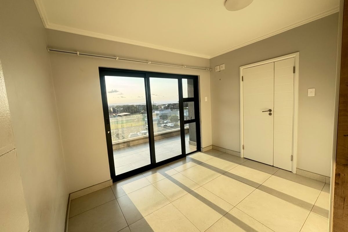 A bright, empty bedroom featuring large sliding glass doors that open to a balcony, tiled flooring, and neutral wall finishes.