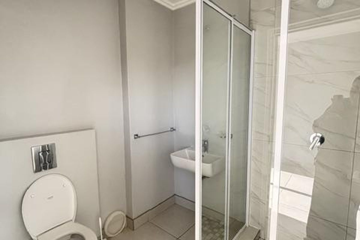 Modern bathroom featuring a wall-mounted toilet, a glass-enclosed shower with marble-look tiling, and a wall-mounted basin.