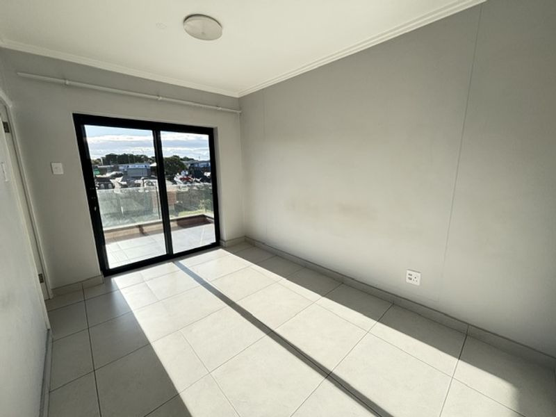 A bright, empty bedroom featuring neutral tiled flooring and a sliding glass door that provides access to an outdoor balcony area.