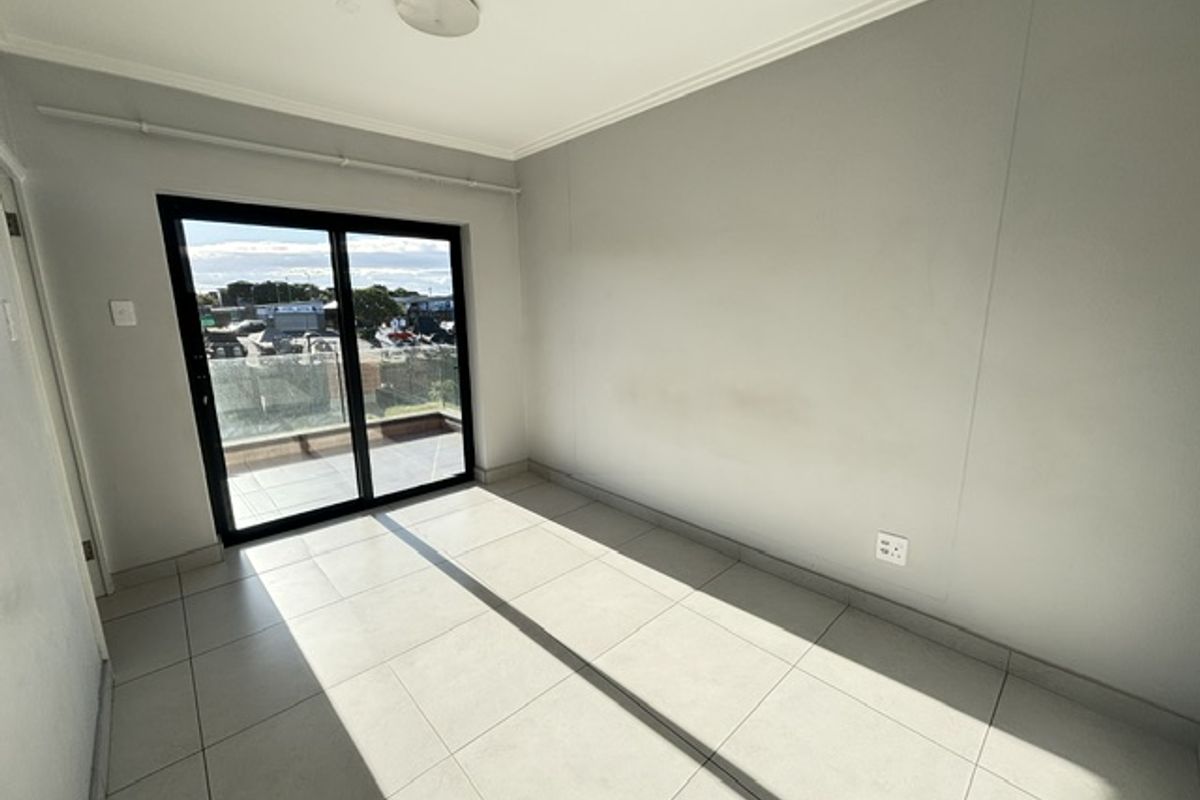A bright, empty bedroom featuring neutral tiled flooring and a sliding glass door that provides access to an outdoor balcony area.