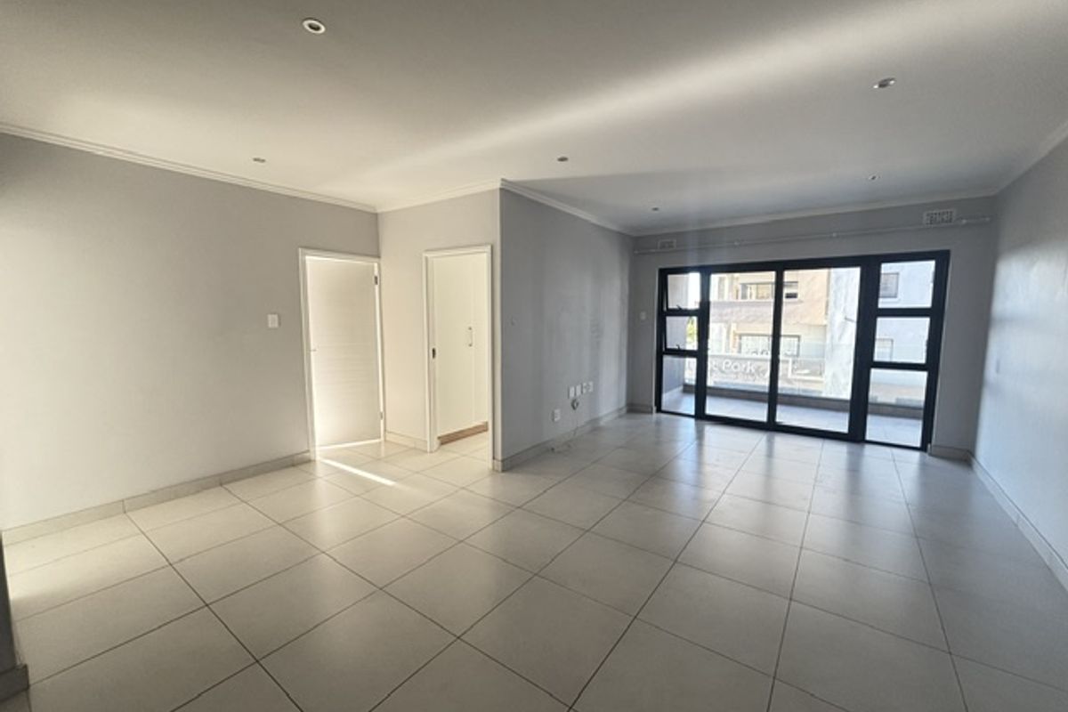 A spacious, empty living area featuring neutral tiled flooring, recessed lighting, and large sliding glass doors leading to an outdoor balcony.
