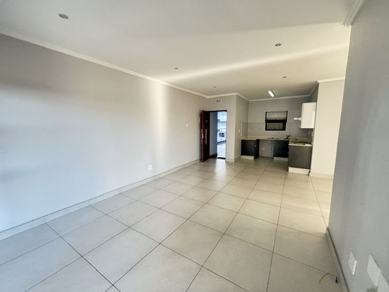 An open-plan living and kitchen area featuring neutral tiled flooring, recessed lighting, and modern kitchen cabinetry in a clean, vacant space.