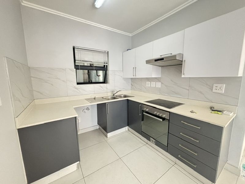 Modern kitchen featuring sleek grey and white cabinetry, stone countertops, integrated electric hob, oven, and extractor fan with contemporary tiled backsplash.