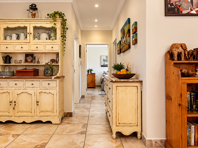 A well-maintained living area featuring neutral tiled flooring, recessed ceiling lighting, and clear sightlines into the adjacent bedroom hallway.