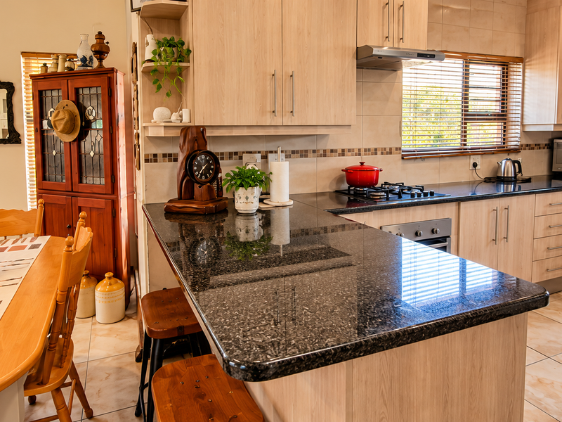 Open plan kitchen featuring light wood cabinetry, dark granite countertops, gas hob, and tiled flooring, seamlessly flowing into the adjacent dining area.