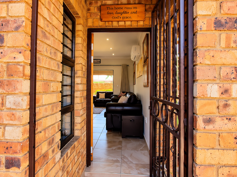 Entrance view featuring face brick exterior, security gate, and a glimpse into the tiled living area equipped with an air conditioning unit.