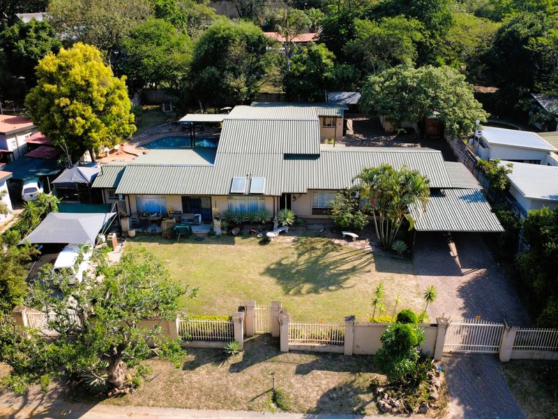 Aerial view of a residential property featuring a metal roof, solar water heater, paved driveway, carport, swimming pool, and established garden.