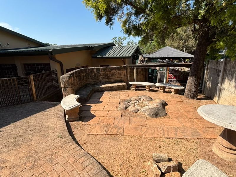 Outdoor patio area featuring built-in stone seating, a central stone fire pit, and paved flooring, providing a rustic space for outdoor entertainment.