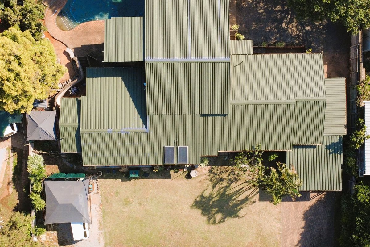 Aerial view of the property showcasing the large corrugated metal roof, swimming pool, expansive garden, and paved driveway access.