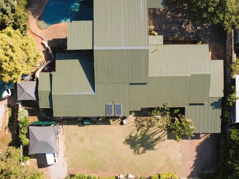 Aerial view of the property showcasing the large corrugated metal roof, swimming pool, expansive garden, and paved driveway access.