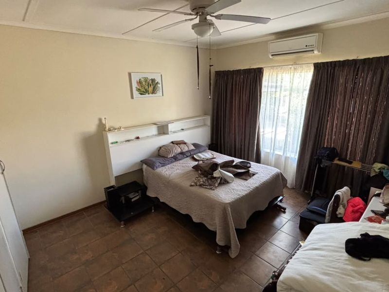 A functional bedroom featuring tiled flooring, built-in cupboards, a ceiling fan, and a wall-mounted split-system air conditioner for climate control.