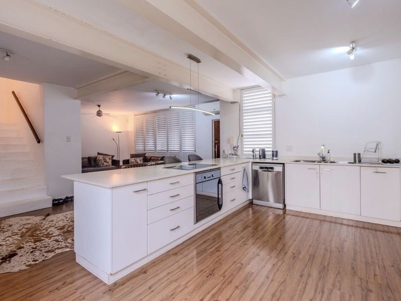 Modern open-plan kitchen featuring sleek white cabinetry, integrated appliances, and laminate flooring, seamlessly flowing into the adjacent living area and staircase.