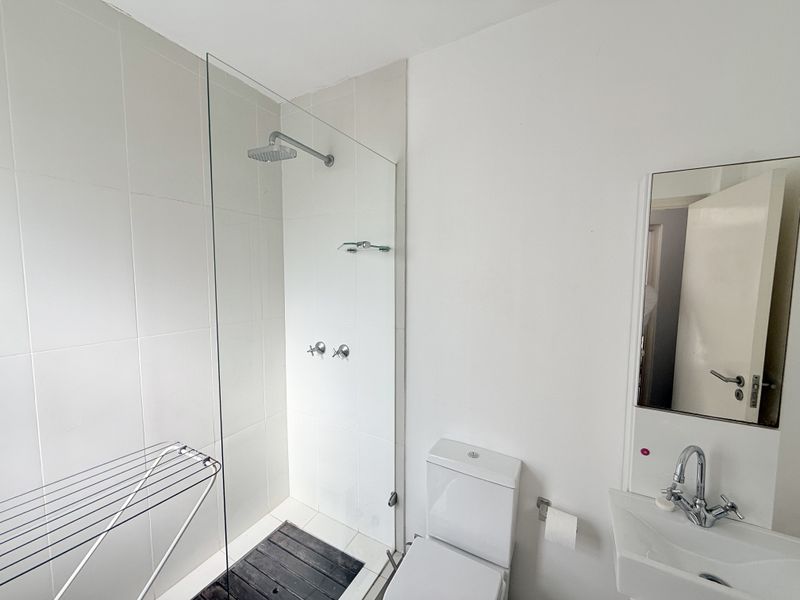 A clean, modern bathroom featuring a glass-enclosed walk-in shower with a rain shower head, a wall-mounted basin, and a toilet.