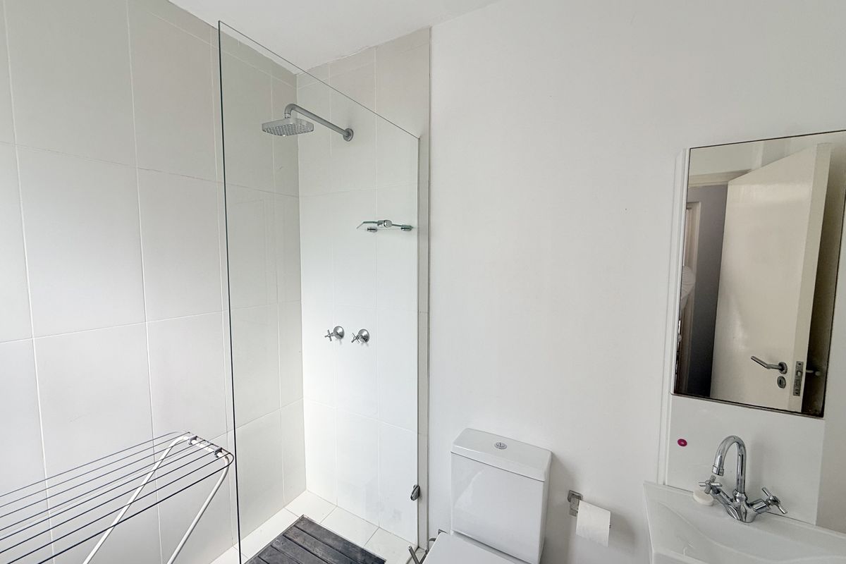 A clean, modern bathroom featuring a glass-enclosed walk-in shower with a rain shower head, a wall-mounted basin, and a toilet.