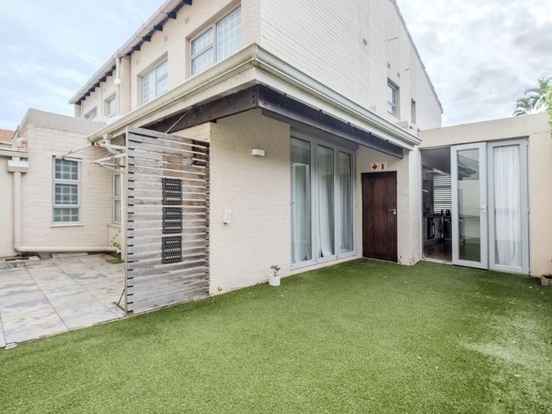 Rear exterior view of the apartment featuring a private patio area, artificial lawn, and direct access through sliding glass doors.