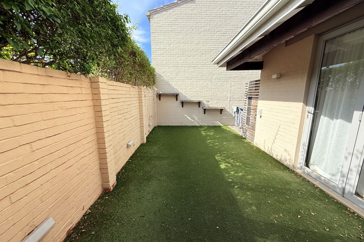 A private rear courtyard featuring artificial turf, a brick boundary wall, and direct access to the interior via sliding glass doors.