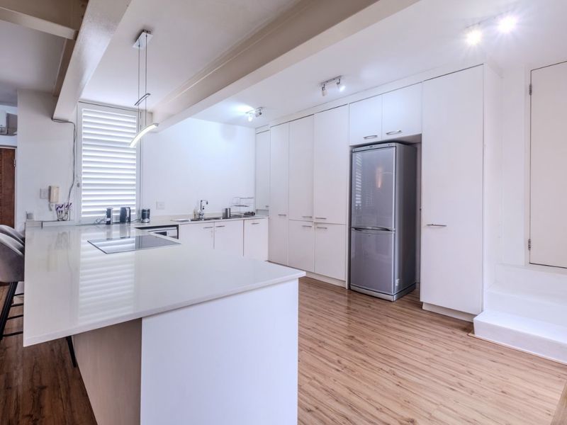 Modern kitchen featuring a central island, sleek white cabinetry, integrated hob, and light wood-look flooring, offering a clean and functional culinary space.