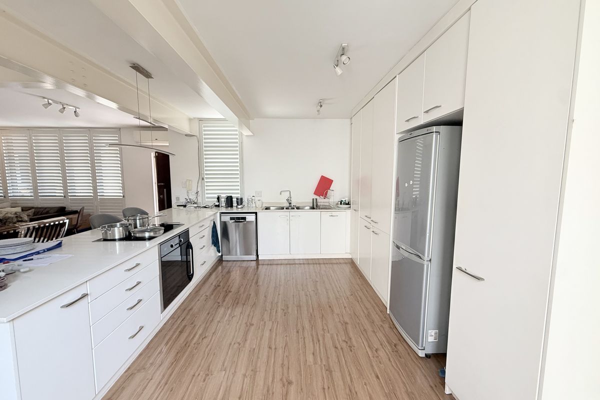 Modern kitchen featuring white cabinetry, integrated appliances, a sleek cooktop, and light wood-look flooring, offering a clean and functional culinary space.
