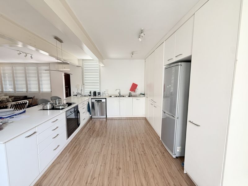 Modern kitchen featuring white cabinetry, integrated appliances, a sleek cooktop, and light wood-look flooring, offering a clean and functional culinary space.