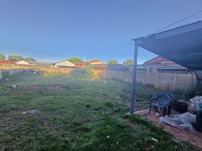 Spacious rear garden featuring a paved patio area with a corrugated metal roof and a precast concrete boundary wall.