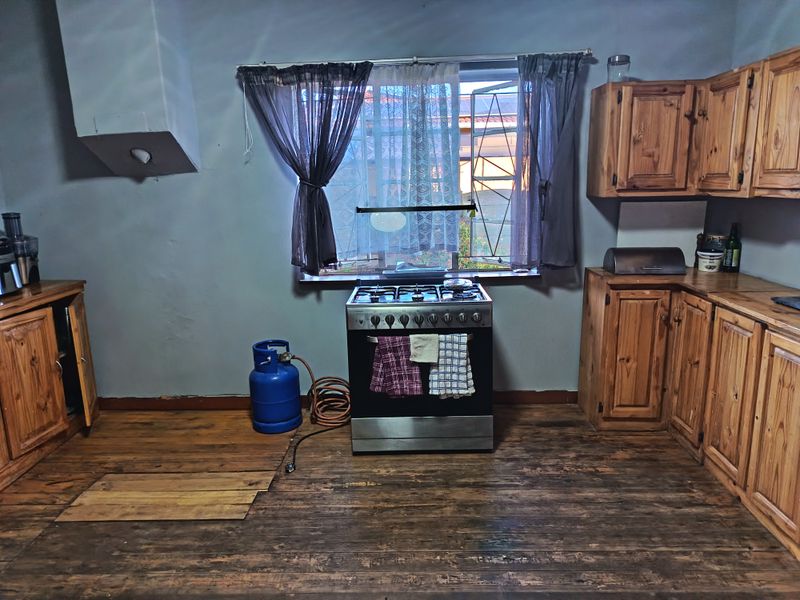 A rustic kitchen featuring wooden cabinetry, a gas stove, and worn timber flooring, offering potential for a modern renovation.