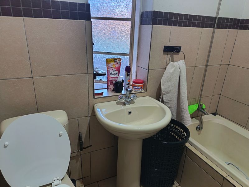A compact bathroom featuring a pedestal basin, bathtub, and tiled walls with a window providing natural light.