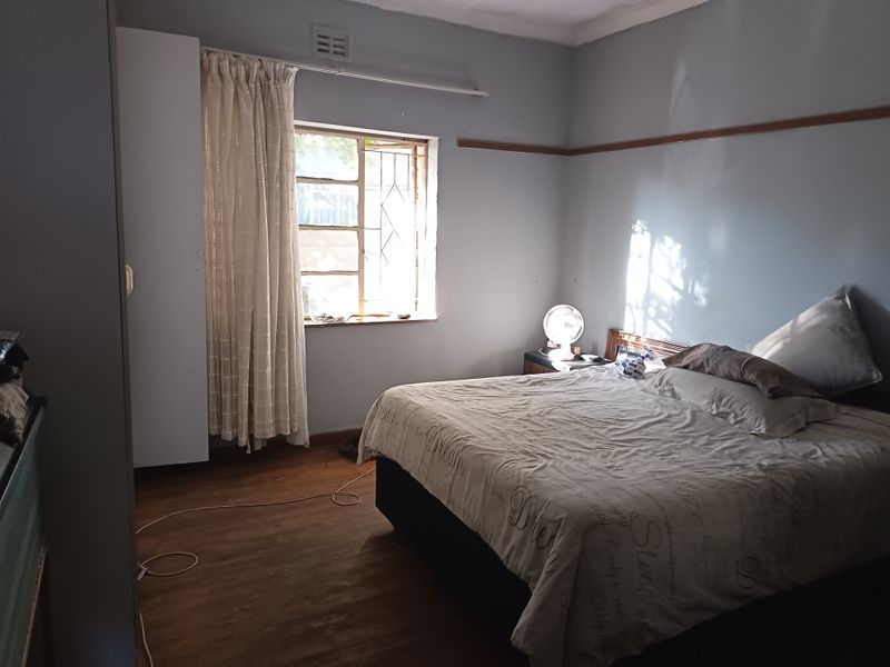 A bedroom featuring timber flooring, a built-in wardrobe, and security bars on the window, offering a functional space with potential for cosmetic updates.