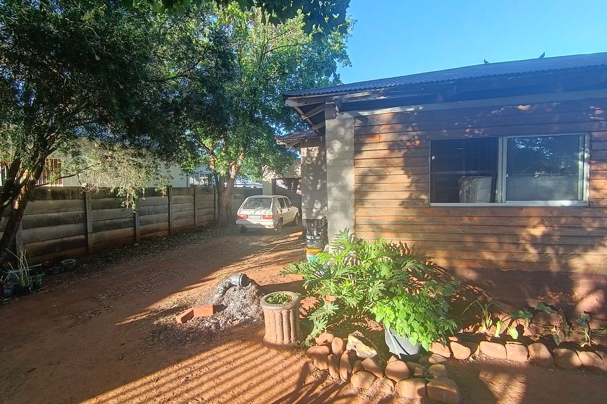Rear exterior view of the property featuring timber cladding, a corrugated metal roof, and a concrete boundary wall.