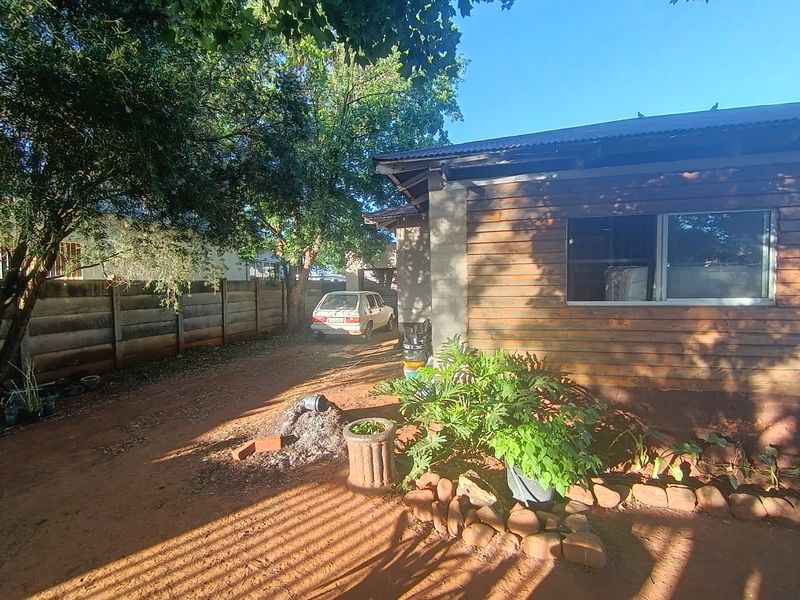 Rear exterior view of the property featuring timber cladding, a corrugated metal roof, and a concrete boundary wall.