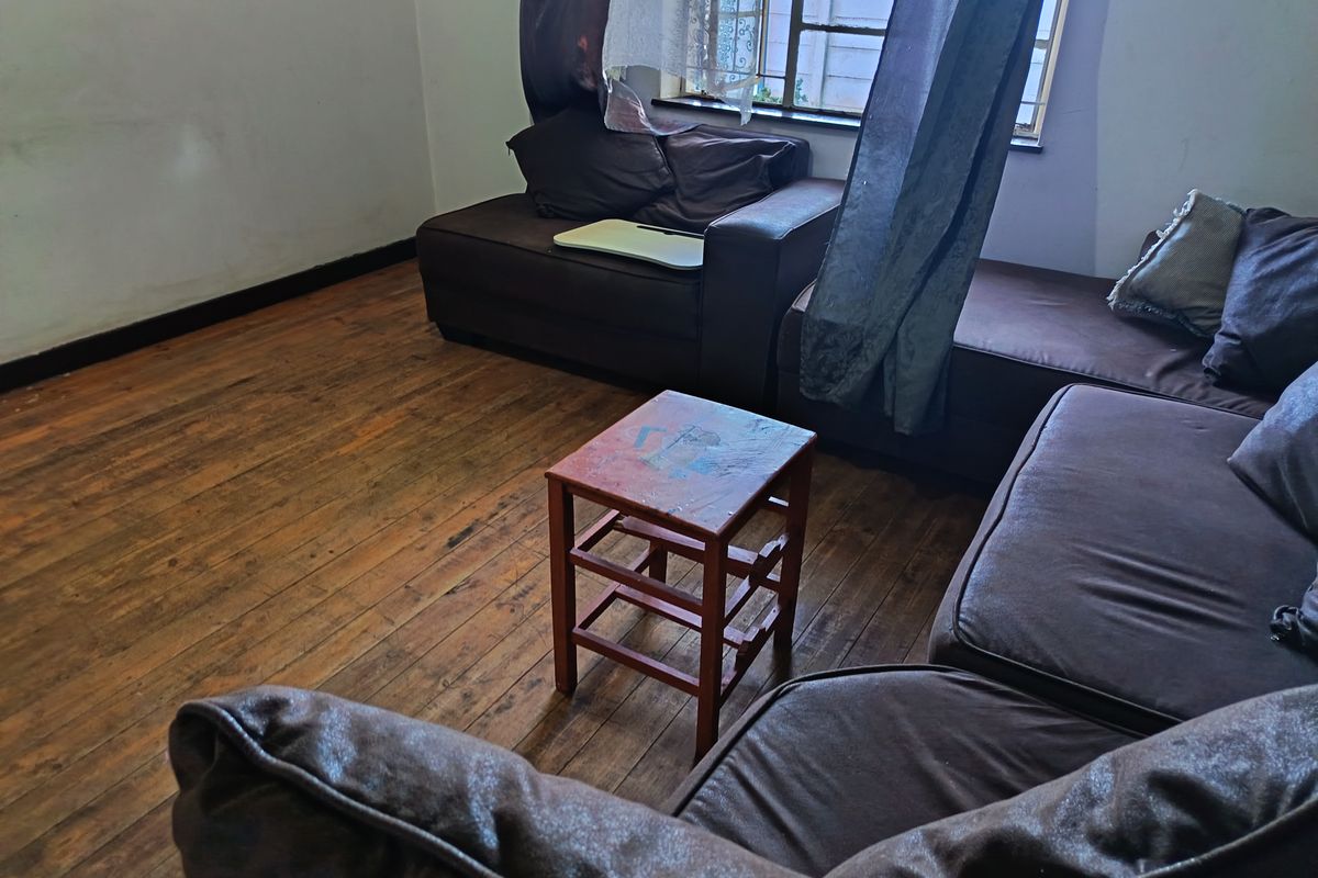 A living room featuring original timber flooring and a steel-framed window, offering a blank canvas for potential interior updates and cosmetic improvements.