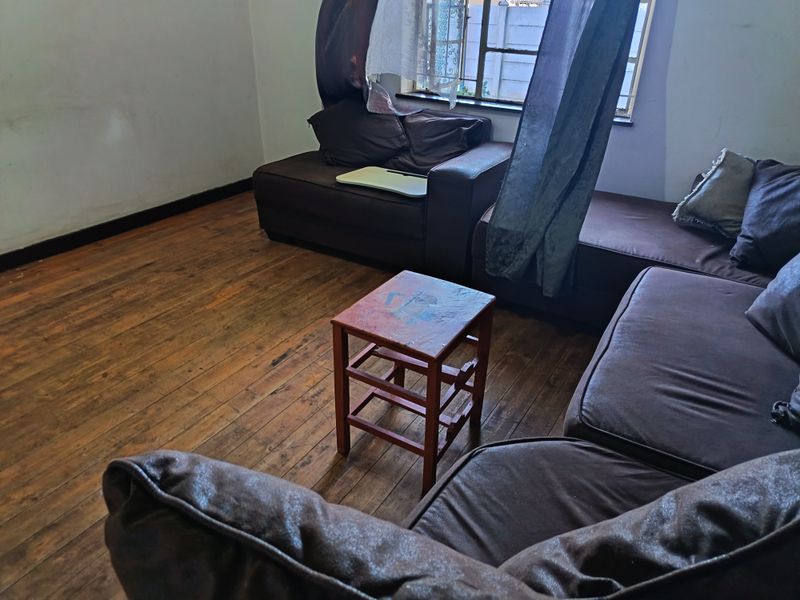 A living room featuring original timber flooring and a steel-framed window, offering a blank canvas for potential interior updates and cosmetic improvements.