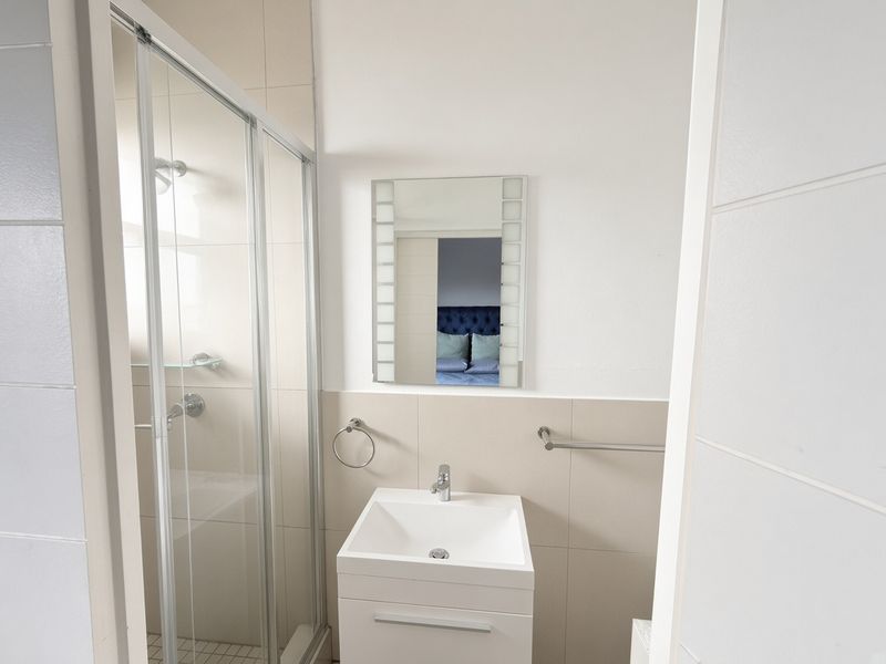 A clean and modern bathroom featuring a glass shower enclosure, a contemporary vanity basin with mixer tap, and a wall-mounted mirror.