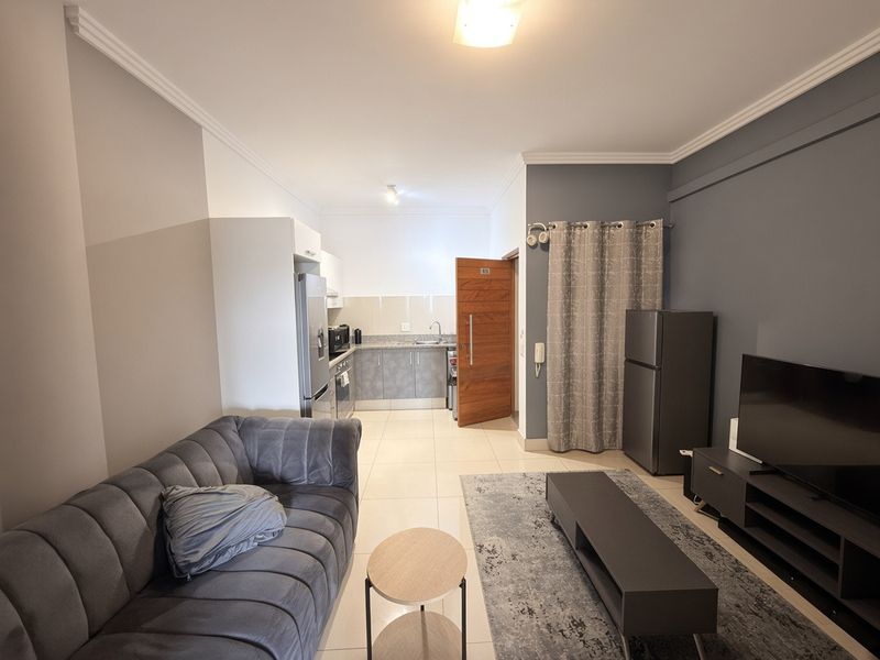 An open-plan living area featuring tiled flooring, crown molding, and a functional kitchen with built-in cabinetry and sink.