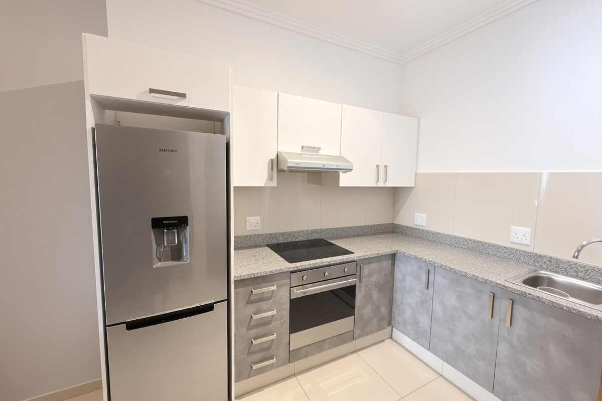 Modern kitchen featuring granite countertops, built-in oven, electric hob, extractor fan, and ample cabinetry, finished with neutral tiled flooring.